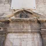 Ne osserviamo l�architrave triangolare finemente scolpita con teste alate a incorniciare l�epigrafe centrale, su cui si impone il bassorilievo di Maria che regge in grembo il corpo esanime del figlio